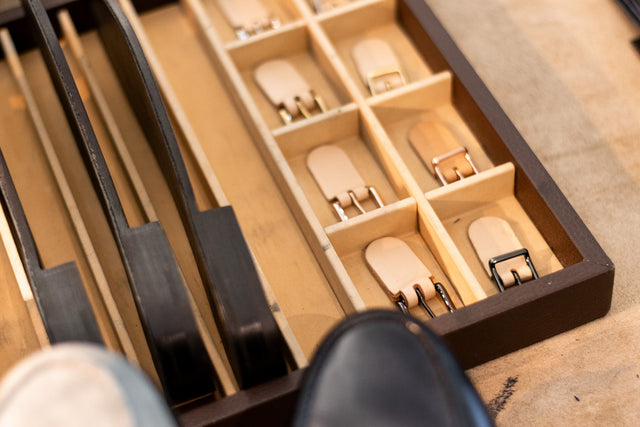 Wooden jewelry box with compartments holding small metal objects on a wooden surface.
