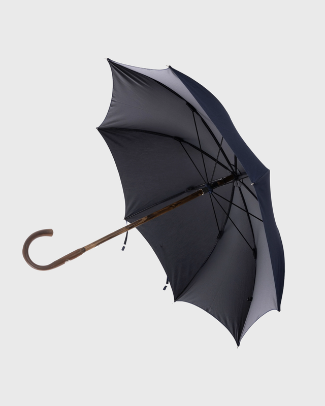 A classic open umbrella with a dark gray and navy blue canopy, a brown wooden handle, and black ribs, shown against a solid light gray background.
