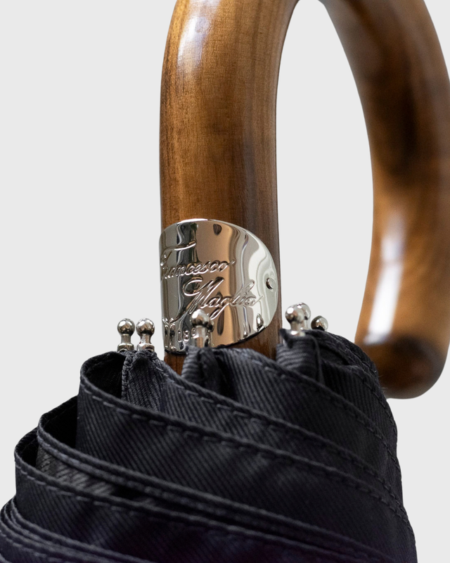 Close-up of a closed umbrella with a curved wooden handle, black fabric canopy, and a polished metal band engraved with the brand name 'Tosciani Napoli'.