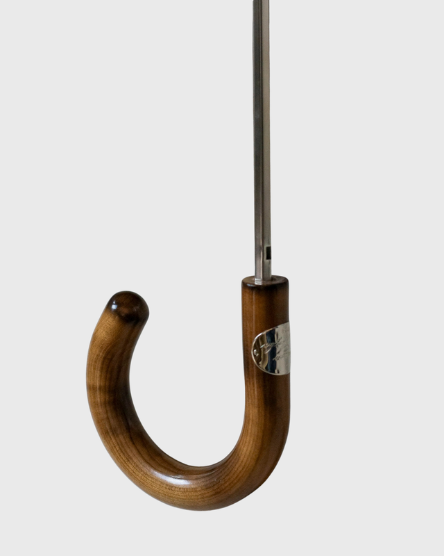 A close-up of a classic J-shaped umbrella handle made of polished brown wood, with a silver metal shaft extending upwards against a light gray background.