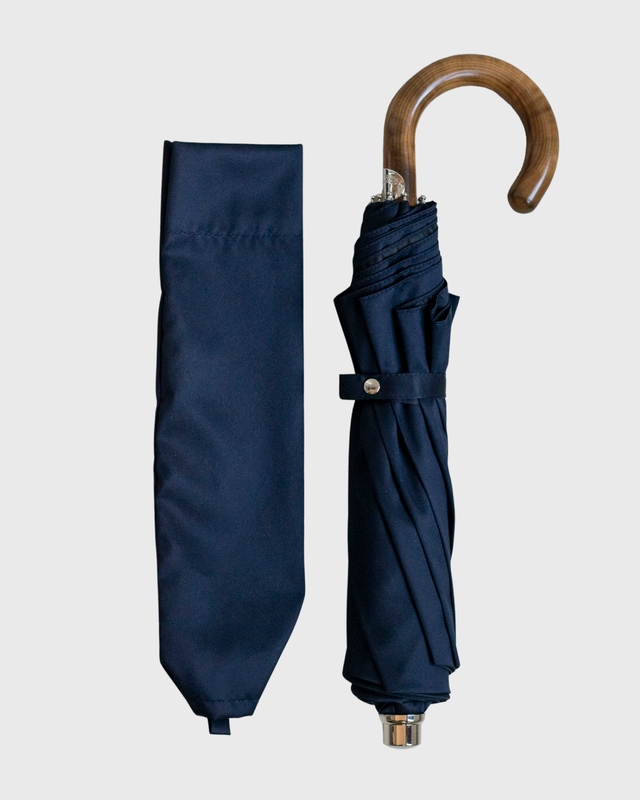 A navy blue umbrella shown alongside its matching fabric cover sleeve, featuring a curved wooden handle and a gold-toned metal tip, set against a plain light gray background.