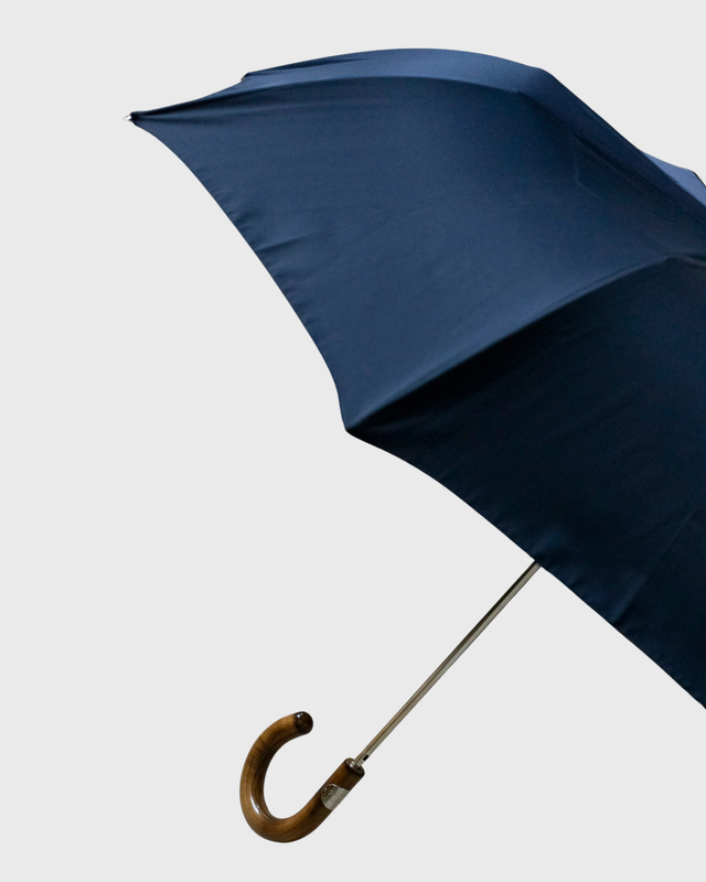 A navy blue umbrella with a curved wooden handle and silver metal shaft, shown against a plain light gray background.